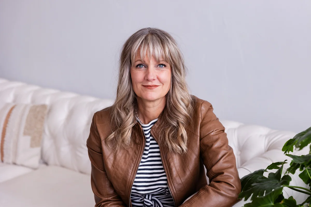 Laura Parker seated on a white couch in a brown leather jacket