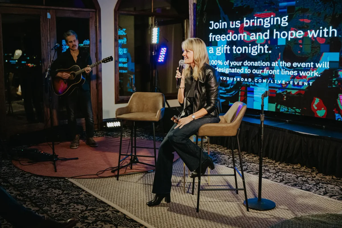 Laura Parker seated on stage, speaking into a handheld microphone at a live event
