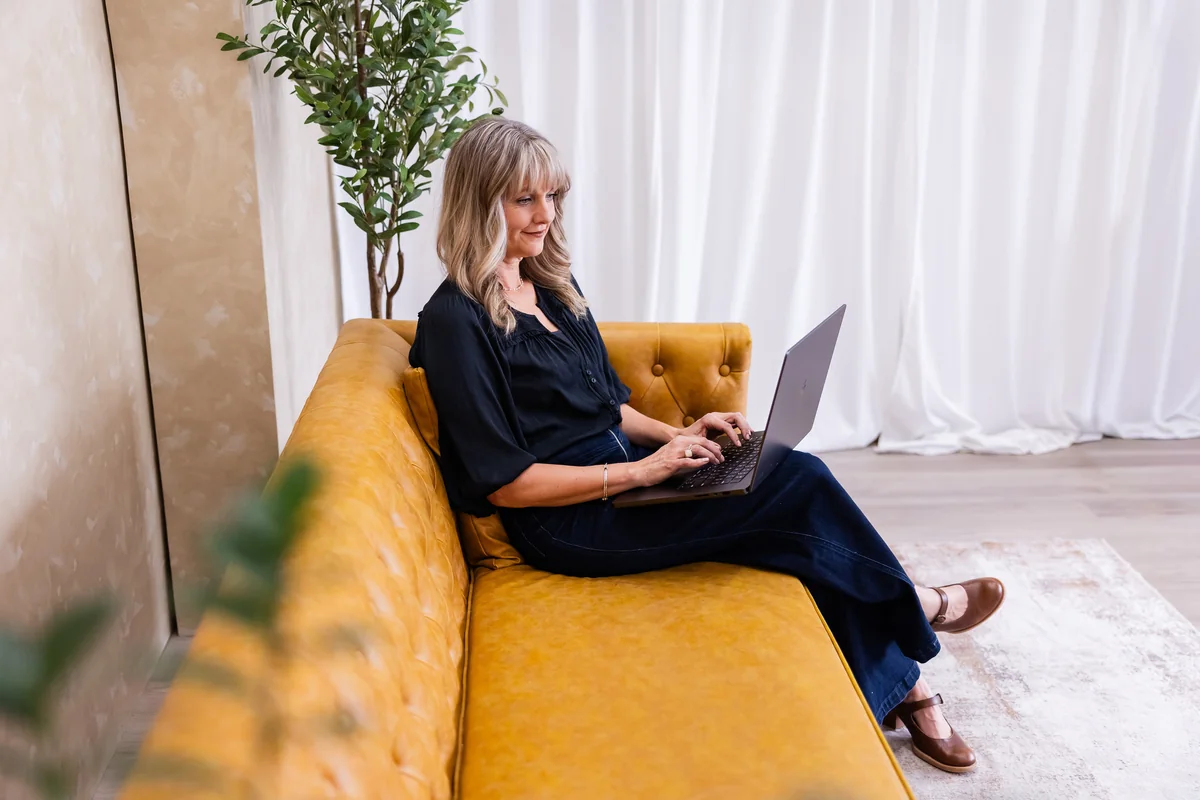 Laura Parker working on a laptop while seated on a yellow couch